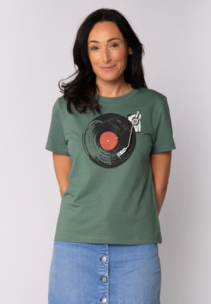 T-shirt en coton vert avec un graphique d'un disque vinyle et d'une cellule. Le design comprend un cercle rouge et des détails d'une platine.