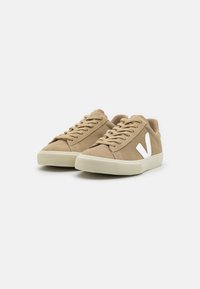 Beige suede sneakers with white rubber sole and distinctive white V logo. Features classic lace-up design and textured outsole for grip.