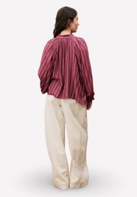 Blouse à manches longues bordeaux rayée avec des plis froncés à l'arrière, associée à un pantalon large crème avec poches latérales et coutures visibles.