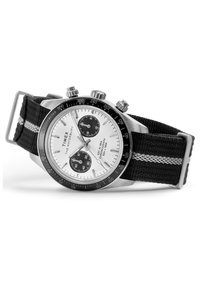 Timex Waterbury kronografur med hvid urskive, sort tachymeter-bezel, to sorte underdialer, sølvfarvede visere og sort stofrem med grå stribe.