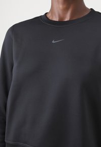Zwarte pullover sweatshirt van zacht materiaal met een ronde hals. Heeft een klein, grijs Nike-logo op de borst. Soepele, lichte textuur.