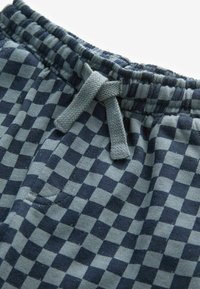 Gros plan d'un pantalon en tissu à carreaux bleu marine et gris avec une taille élastique et un cordon gris noué.