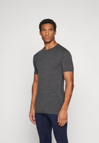 T-shirt de manga curta, justo, feito de um tecido texturizado de cor cinza escuro, com um decote redondo, combinado com calças de desporto em azul marinho.