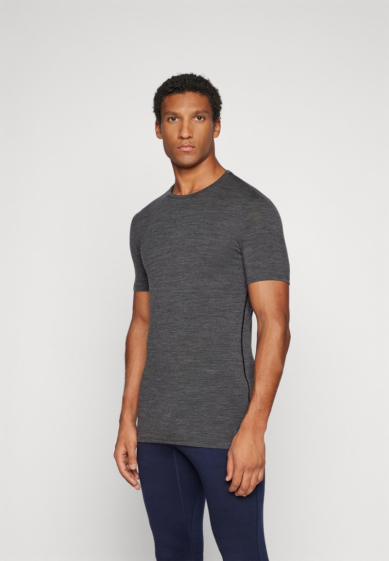 T-shirt de manga curta, justo, feito de um tecido texturizado de cor cinza escuro, com um decote redondo, combinado com calças de desporto em azul marinho.