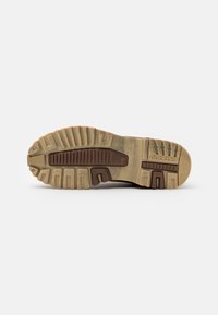 Suela de zapato con un patrón de goma marrón y crema texturizado, que presenta profundas ranuras para tracción y un logo de marca en el lateral.