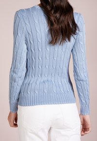 Vaaleansininen neulepusero, jossa on palmikkokuvio, ribbireunat hihoissa ja helmassa, pitkät hihat ja klassinen pyöreä kaula-aukko.