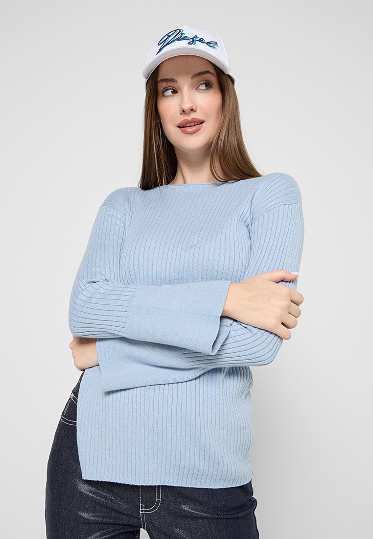 Hellblauer, gerippter Pullover mit langen Ärmeln und rundem Ausschnitt, aus strukturiertem Stoff mit breiten Bündchen. Kombiniert mit einer weißen Mütze.