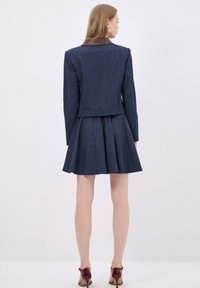 Námořnické pruhované sako s hnědým koženým límcem, spárované s rozšířenou sukní. Hladká textura a přizpůsobený střih, který ukazuje na obepínající design.