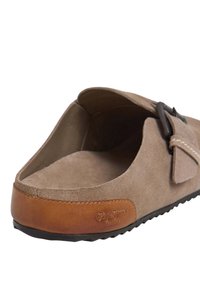 Brun mockaskosläpp med en tan läderdetalj och svart gummisula, med en spänndetalj och slät textur.