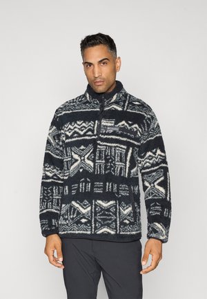 Fleece pullover in navy with white geometric patterns, half-zip neck, high collar, and patch pocket. Soft texture and relaxed fit.