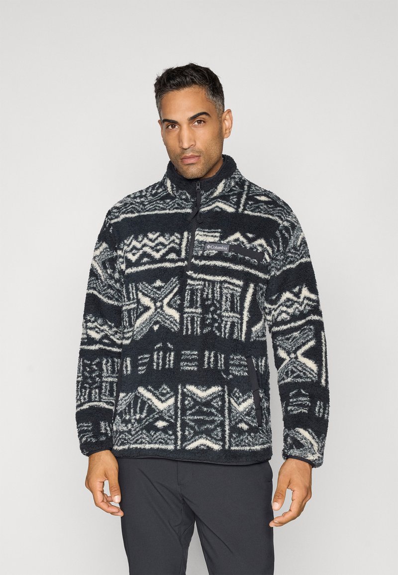 Sötétkék fleece pulóver fehér geometriai mintákkal, fél cipzárral, magas gallérral és patkó zsebbe. Puha tapintású és laza szabású.