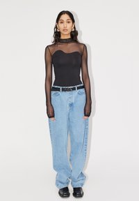 Body nera con maniche lunghe trasparenti e scollatura a cuore, abbinata a jeans in denim blu chiaro a vestibilità ampia e scarpe nere.