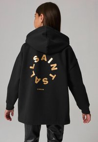 Sudadera negra con un gráfico circular dorado que incluye el texto "SAINT LONDON" en la parte trasera. Tiene un corte holgado y capucha.