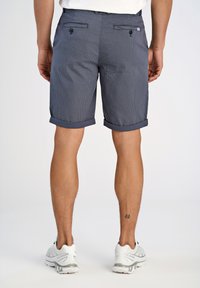 Pantaloni corti a quadri blu scuro con risvolti, due tasche posteriori con bottoni e texture liscia, abbinati a scarpe da ginnastica bianche.