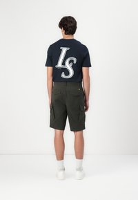T-shirt en coton bleu marine avec un grand graphisme blanc "LS" dans le dos, associé à un short cargo vert olive et des baskets blanches.