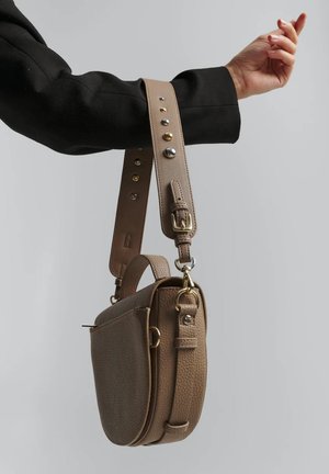 Sac bandoulière beige avec une surface texturée, une petite poignée supérieure et une bandoulière amovible ornée de clous métalliques et de boucles décoratives.