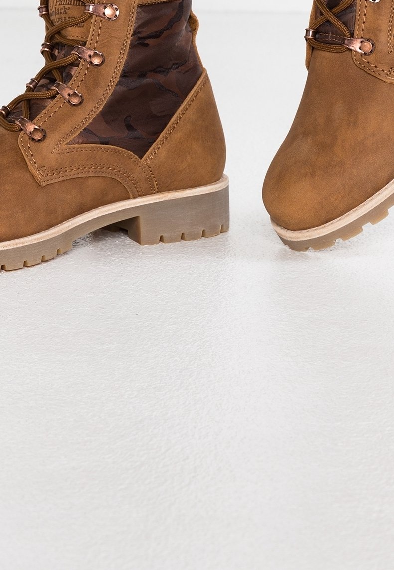 Bottes bottines en daim marron avec une insertion en tissu camouflage, dotées d'une semelle robuste et texturée ainsi que d'œillets métalliques pour les lacets.