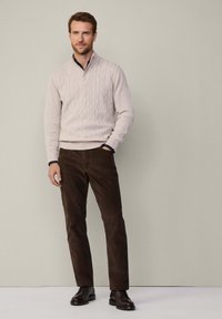 Hellbeige Kabelstrickpullover, dunkelbraune Cordhosen und schwarze Lederschuhe. Einfaches, klassisches Design mit gerippten Akzenten.