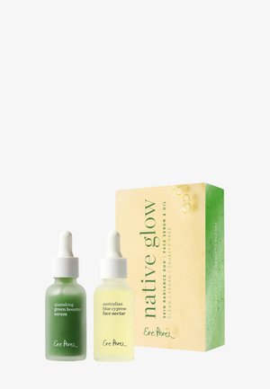 Zwei Pipettenflaschen mit der Aufschrift Hautseren, grün und gelb, neben einer Schachtel mit der Aufschrift "native glow" für ein Gesichtserum- und Ölset.