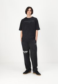 Black T-shirt with "FOREVER FORWARD" text, paired with black sweatpants featuring "MCLAREN" logo. Both garments are loose-fitting.