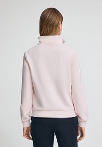 Ljusrosa sweatshirt med hög krage, långa ärmar, ribbade muddar och nederkant, tillverkad av mjukt tyg. Enkelt design, inga synliga mönster eller detaljer.