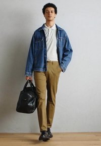 Jeansjakke, hvid polo skjorte, beige bukser, sorte sko og en sort lædertaske. Modellen står foran en neutral baggrund.
