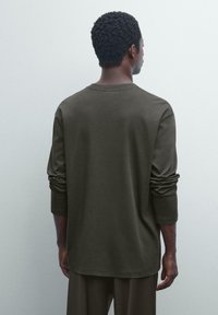 Dunkelolivgrünes Langarm-T-Shirt mit rundem Halsausschnitt, lockerem Schnitt und gesäumten Ärmeln, aus weichem, strukturiertem Baumwollstoff gefertigt.