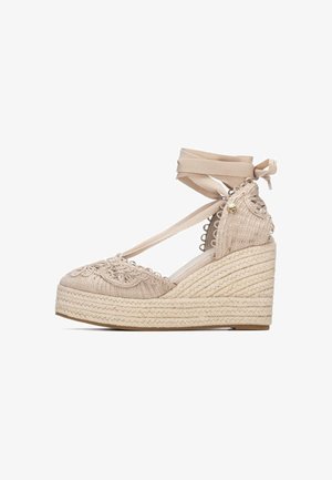 Espadrillas beige con zeppa, suola intrecciata in corda, dettagli in pizzo e cinturini alla caviglia legati con un fiocco sul retro.