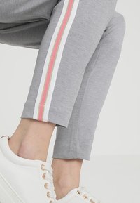 Grå träningbyxor med vit, rosa och guld randig sidodetalj. Har en slim fit och ruggad textur. Matchas med vita sneakers.