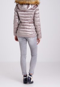 Metallic sølv pufferjakke med en aftagelig tan pelshætte, ribbede manchetter og lynlåslommer, iført med tætsiddende lysegrå jeans og ankelstøvler.