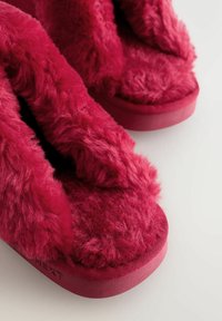 Puha, világospiros papucsok puha textúrával, lapos talppal és nyitott orrú kialakítással. Sima gumitalp márkás részlettel.