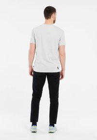 Lichtgrijze T-shirt met korte mouwen en een relaxed fit, gecombineerd met zwarte jeans en witte sneakers met groene accenten.