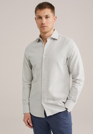 Camisa de manga larga gris claro con cuello abotonado, que presenta una textura sutil y botones blancos, combinada con pantalones oscuros a rayas.