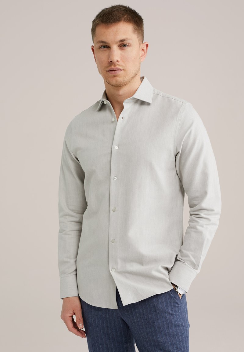 Maglietta a maniche lunghe grigio chiaro con colletto a camicia, caratterizzata da una texture sottile e bottoni bianchi, abbinata a pantaloni scuri a righe sottili.