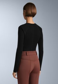 Black long-sleeve top with a fitted design and raglan sleeves, paired with high-waisted brown pants featuring textured detailing and a belt.