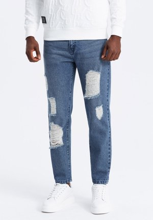 Vaqueros de mezclilla de color azul claro con grandes parches rasgados. Presentan un diseño de pierna recta y un acabado desgastado. Combinados con zapatillas blancas.