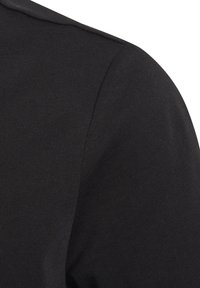 Black ribbed fabric, featuring a smooth texture with a fitted design. The image captures a close-up of the shoulder area.