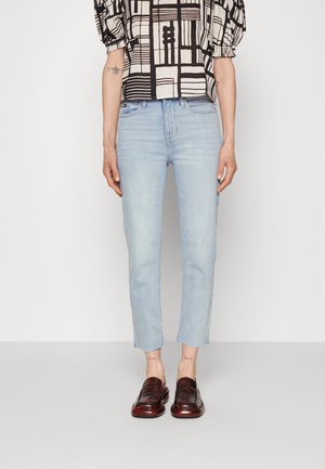 Osoba ubrana w jasnoniebieskie krótkie dżinsy, czarno-białą bluzkę w wzory z bufiastymi rękawami oraz ciemnobrązowe skórzane lordsy.