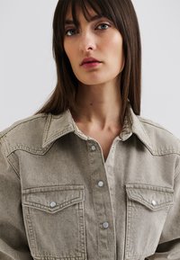 Vaaleanharmaa denim-paita napitetulla etuosalla, jossa on kaksi rintataskua, terävä kaulus ja erottuva ompelu. Pehmeä rakenne.