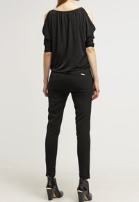 Haut noir décolleté avec un tissu drapé et des accents dorés ; associé à un pantalon noir ajusté et des bottines à talons.