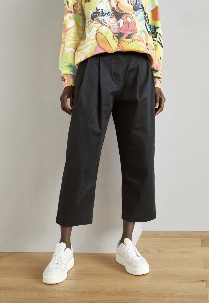 Pantalons noirs raccourcis en coton, avec un design plissé, associés à des baskets blanches et un sweat-shirt graphique coloré.