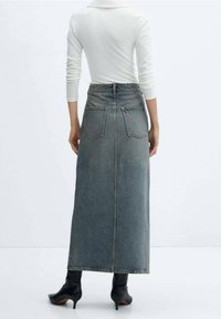 Džínová sukně s vysokým pasem, dlouhá a modré barvy. Obsahuje dvě zadní kapsy a detail bočního švu. Nosená s černými podpatkovými botami.