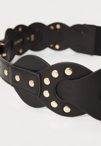Cinturón de cuero negro con diseño ondulado y tachuelas y herrajes en tono dorado. Textura suave; cierre ajustable.