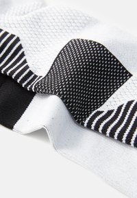 Tejido texturizado que presenta una mezcla de patrones en blanco y negro, incluyendo malla, rayas y un acabado suave, mostrando contrastes de color distintivos.