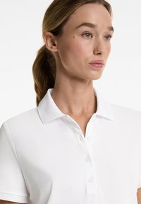 White polo shirt featuring a classic collar, five-button placket on the front, and a smooth, textured fabric.