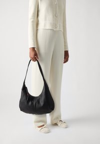 Borsa a spalla in pelle nera con forma arrotondata, cinturino singolo e dettagli zipper sottili. Texture liscia con accenti di cuciture leggere.