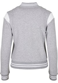 Sweatshirt gris avec des poignets et un ourlet côtelés, ornés de bandes blanches sur les épaules et le col. Tissu doux et texturé avec une coupe décontractée.