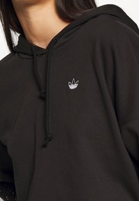 Felpa nera con cappuccio realizzata in materiale morbido, con un piccolo logo a tre strisce ricamato sul petto e chiusura con coulisse.