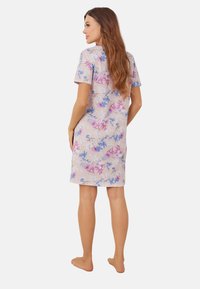 Kwiatowa nocna sukienka do kolan w jasnoróżowym kolorze, z niebieskimi i fioletowymi wzorami roślinnymi, krótkimi rękawami i luźnym krojem.