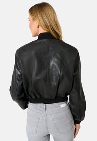 Giubbotto bomber in pelle nera con vita e polsini a costine. Caratterizzato da una texture liscia e una silhouette arrotondata, progettato per un fit rilassato.